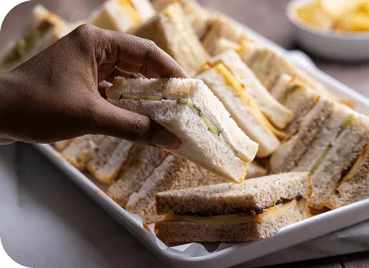 Wenzel’s Veggie Sandwich Platter with a cream cheese and cucumber sandwich held up from the tray